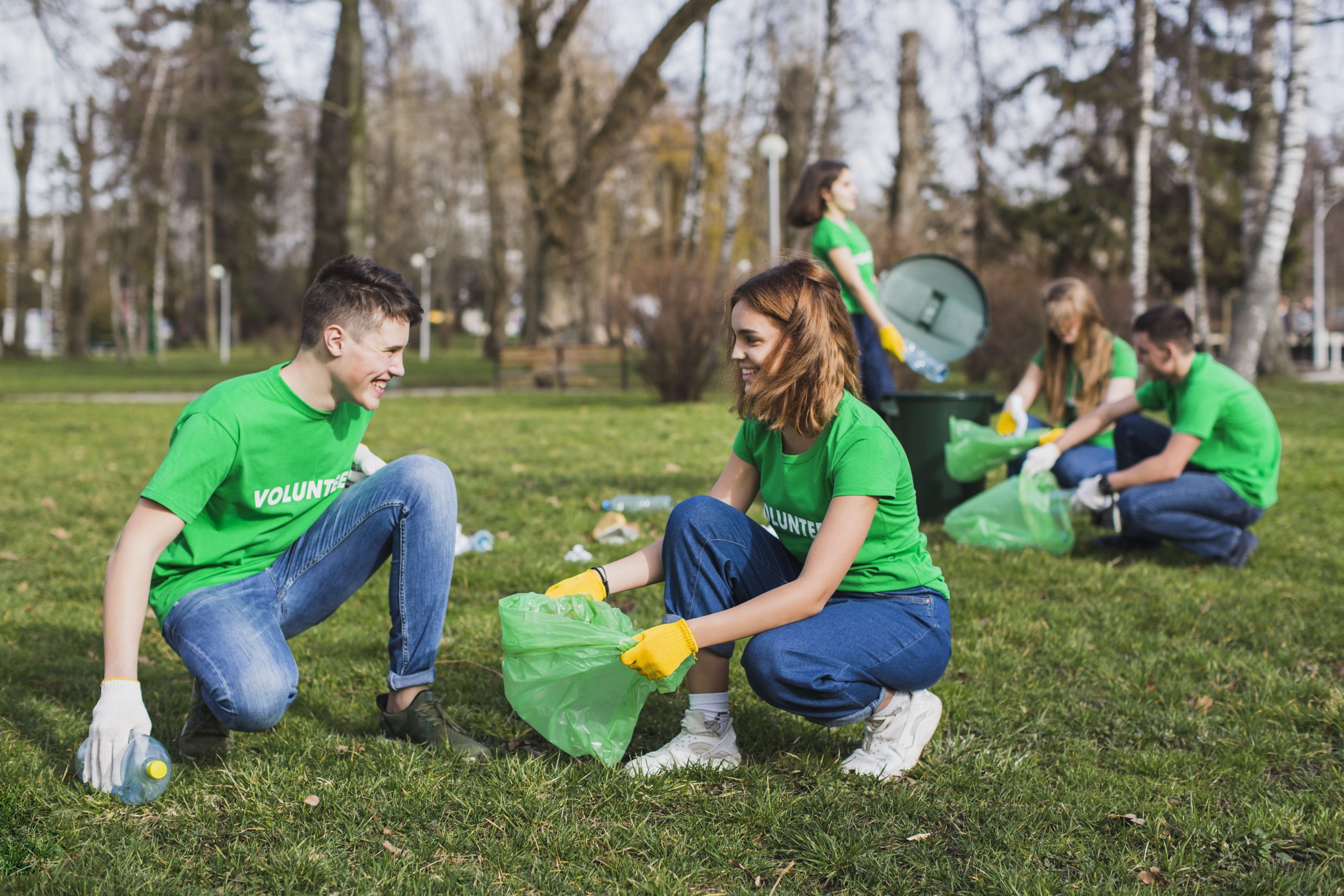 Group of young volunteers wearing green shirts and gloves collecting garbage in a park to promote environmental cleanliness