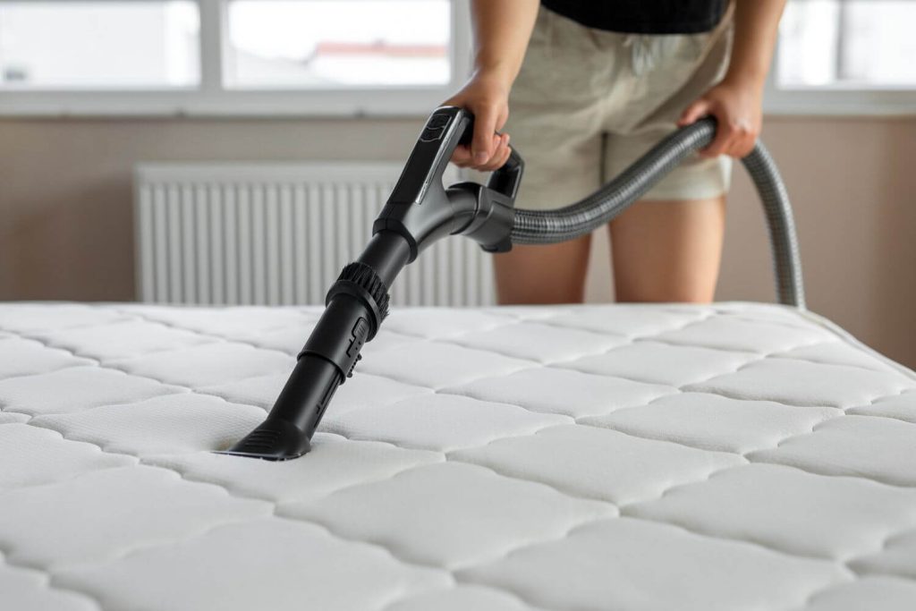 Professional vacuuming of a white quilted mattress using specialized equipment for deep cleaning and germ elimination in Ajman.